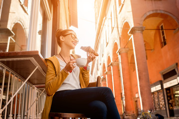 Young woman having italian breakfast with croissant and coffee at the cafe on the street in Bologna city. Soft focus with small depth of field