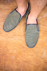 Man wearing a pair of old green shoes on wooden floor