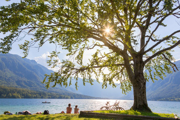 Wall Mural - Active sporty couple relaxing on lake beach after active day of cycling enjoying beautiful nature around lake Bohinj, Slovenia.