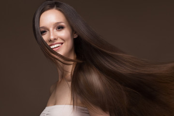 Beautiful brunette girl in move with a perfectly smooth hair, and classic make-up. Beauty face. Picture taken in the studio.