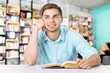 © Africa Studio - Young man with book on blurred book shelves background.