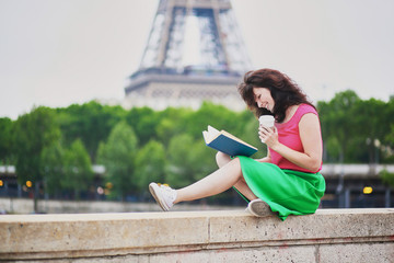 Wall Mural - Girl with coffee to go reading a book near the Eiffel tower.