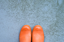Used, Dirty, Orange Rubber Wellington Boots On A Grungy Concrete Surface With Lots Of Copy Space, Top View, Horizontal