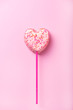 white chocolate marshmallow in heart shape, decorated with lots of pink and orange colored sugar bonbons, isolated on a pink background, vertical, with copy space