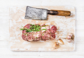 Wall Mural - Raw uncooked roastbeef meat cut with rosemary, thyme and garlic and butcher knife on old white painted wooden background, top view, horizontal composition