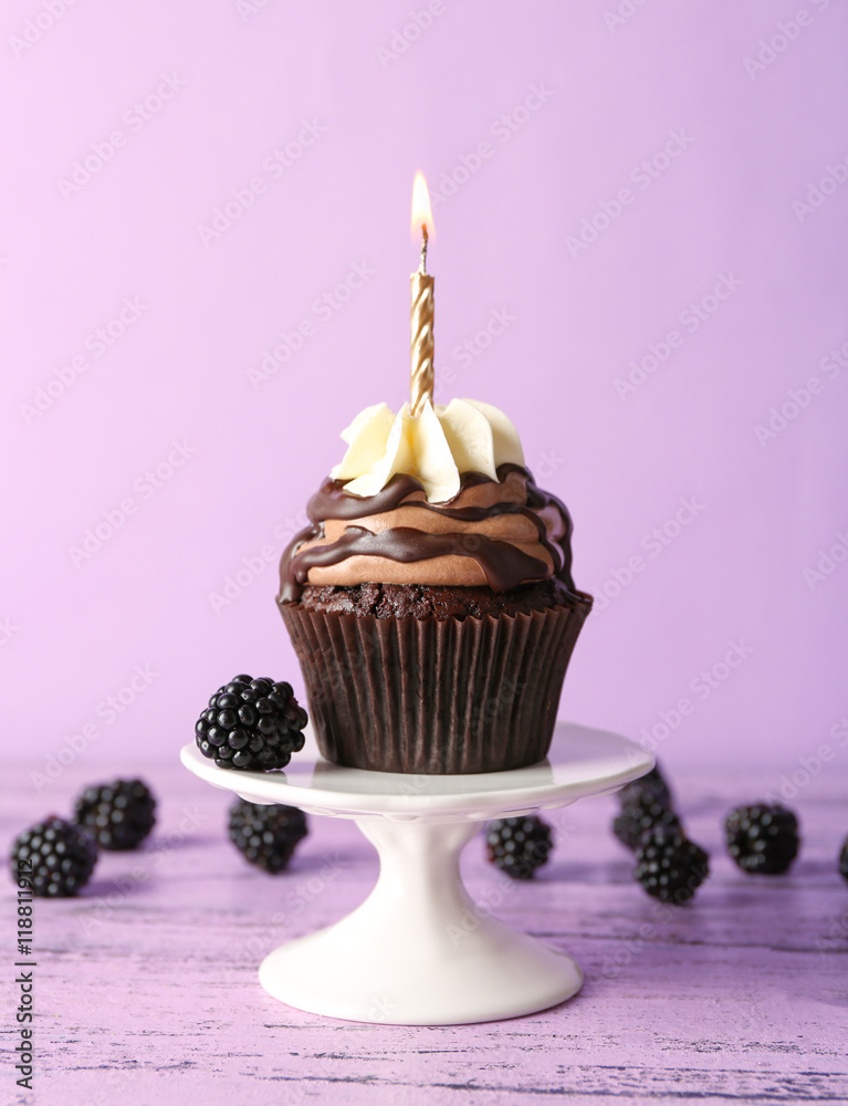 Tasty chocolate cupcake with berries and candle on purple background