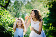© barbiturat - Mother and daughter blowing soap bubbles in the park