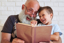 Bearded Aged Man And His Grandson Having Fun Reading A Book Toge