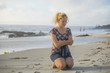 Cold shivering Young blonde woman sitting holding thermos on beach in California with eyes closed