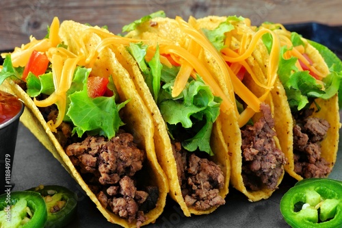 Group of hard shelled tacos with ground beef, lettuce, tomatoes and cheese close Plakát