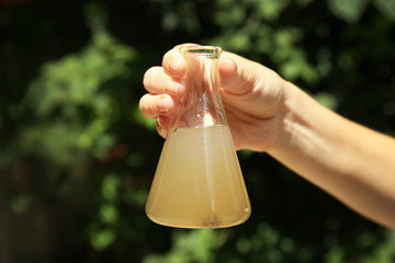 Sticker - Female hand holding flask with contaminated water on blurred nature background