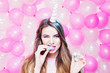 Cute young woman with unicorn horn eating colorful marshmallow. Pastel tones