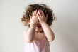 © Natalie Board - Toddler girl with curly hair with hands covering face playing peekaboo against neutral background