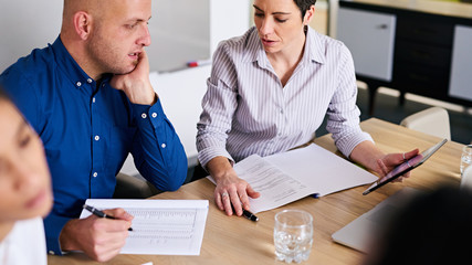 Mature businesswoman asking her male business colleague for clarification on his work in the company's latest financial reports where she feels more details are required.