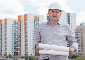 An engineer with construction plans on a background with buildings