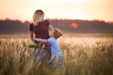 Cute kid boy hugging his mother on a summer meadow on beautiful summer sunset. Happy family together. Mum and child. Motherhood and childhood. Family walking in the field. Outdoors.