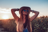 Fototapeta Boho - Girl in a cowboy hat in a sunflower field. Sunset