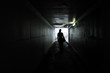 Silhouette of a young woman walks alone in a dark tunnel
