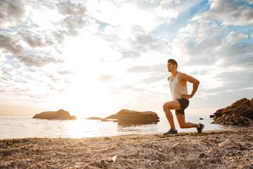 Wall Mural - Young healthy man athlete doing squats at the beach