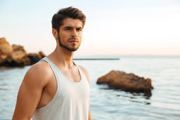 Young handsome man athlete standing at the rocky beach by