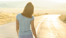 Young Woman Walking Away On An Empty Road