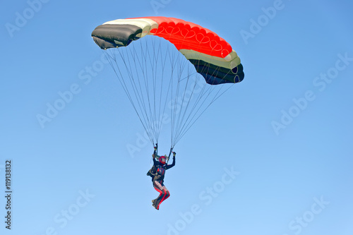 Fotografie, Obraz Paraglider flying on colorful parachute in blue clear sky at a bright sunny summer day