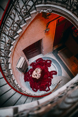 Beauty and shape. Young beautiful woman standing on old round staircase. Blonde girl with tatoo in red cloud dress embracing. Advertising picture