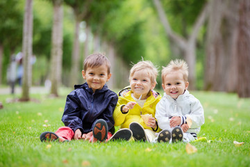 three young boys sitting on the grass in a park and smiling, the boy in the middle eating ice cream