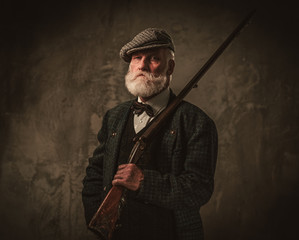 senior hunter with a shotgun in a traditional shooting clothing, posing on a dark background.