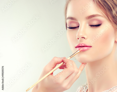 Hand of make-up master, painting lips of young beautiful model Plakat