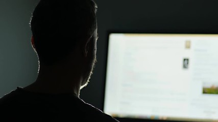 man surfing the web internet at night in a dark room as seen from behind  backlit pan