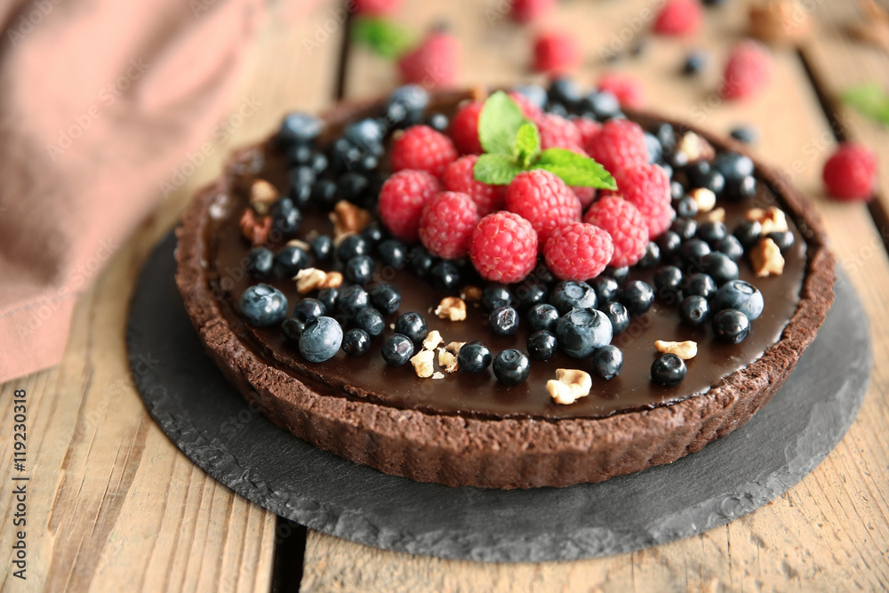 Delicious chocolate tart with berries and nuts on slate plate, closeup