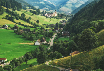 Wall Mural - Scenic travel background: green summer mountain landscape with forests, fields and old church in Germany, Black Forest