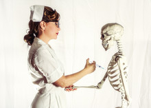 Vintage Nurse Giving A Skeleton A Shot. Classic Female Nurse In Authentic Vintage Uniform Giving A Skeleton A Shot. Edited In A Vintage Film Style.