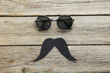 Wall Mural - Black sunglasses and mustache on a grey wooden table