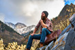 happy bearded guy sitting on luggage at top of mountain