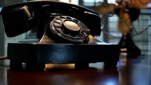 An Old Rotary Dial Telephone With Out Of Focus Vintage Electric Fan Turning In The Background.