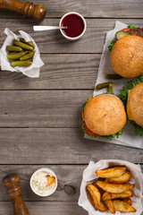 Poster - different hamburger on wooden table with sauces, fries and pickl