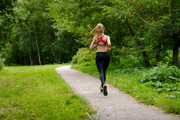 Wall Mural - Young slim woman jogging in a park