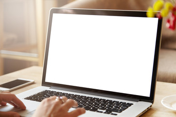 Portrait of young Caucasian female freelancer typing messages via email, using laptop computer and mobile phone for distant work while sitting at coffee shop. Woman browsing Internet at home