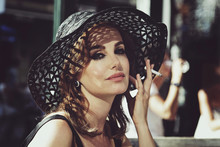 Jolie Femme Brune Style Années 1960 En Robe Noire Et Chapeau Vintage Fumant Sur Une Terrasse Au Soleil