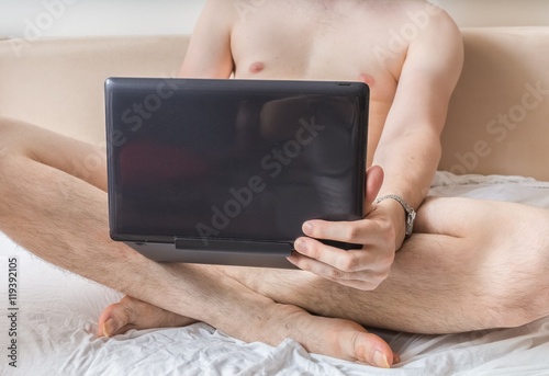 Plakat Młody nagi mężczyzna ogląda pornografię na laptopie i masturbuje się.
