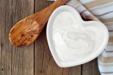 Wall Mural - Greek yogurt in a heart shaped bowl, overhead scene against a rustic wood background