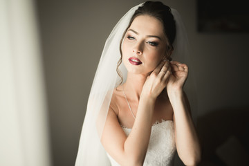 Beautiful young bride with makeup and hairstyle in bedroom, newlywed woman final preparation for wedding. Happy girl waiting groom. Portrait soft focus