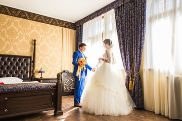 happy luxury bride and groom standing at window light in rich room