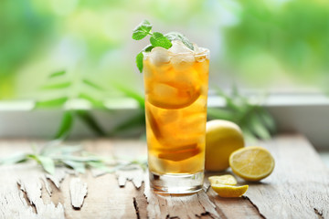 Canvas Print - Glass of iced tea on wooden table and blurred green background