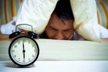 sleeping asian young male disturbed by alarm clock early morning on bed