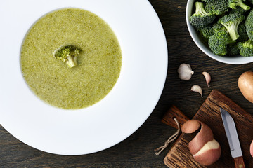 Wall Mural - White plate with broccoli soup and ingredients on dark wooden background