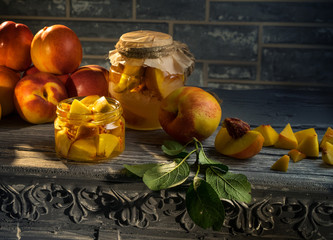 On a wooden table there are two jars of peach preserves. This homemade jam. Around a lot of fresh peaches.