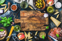 Italian Food Cooking Ingredients On Dark Background With Rustic Wooden Chopping Board In Center, Top View, Copy Space